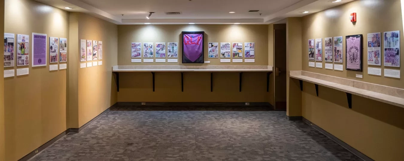 Art gallery with framed pictures on beige walls, focused lighting, and carpeted floor. Central artwork features a large purple shape.