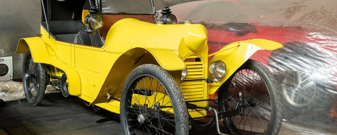 Yellow vintage car with three wheels in a dimly lit garage.