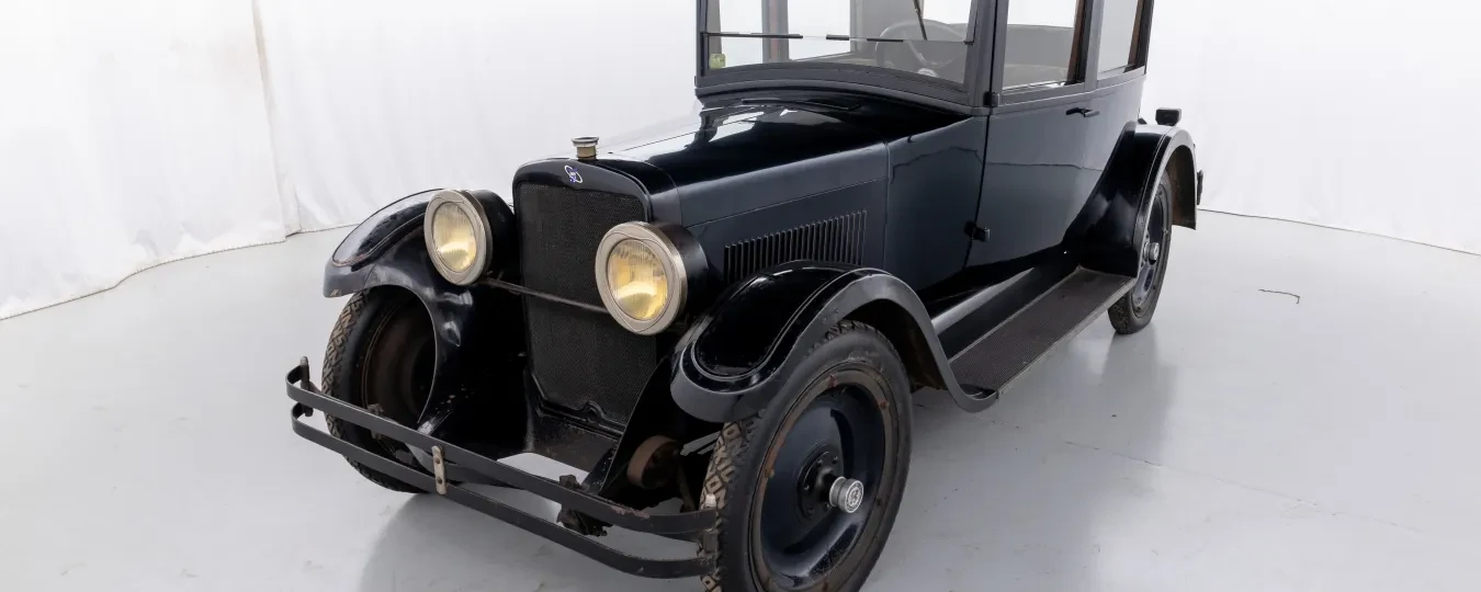 Dark vintage car with round headlights in a white studio setting.