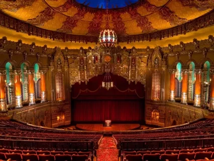 Interior of the Fox Theater in Detroit, from the perpective of the audience. Showing dark red velvet seats, Arabian inspired architechture with gold accents.