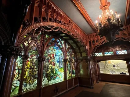 Gothic Room at the Dossin Great Lakes Museum, an ornate room with wood carved arches, a chandelier, and a stained glass window depicting Cadillac's arrival in Detroit.