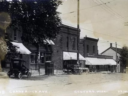 Historic street scene with vintage buildings, cars, and horse-drawn wagon under an overcast sky.