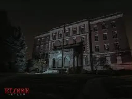 Dark, eerie photo of a large, old brick building at night, dimly lit with a hint of light on the facade.