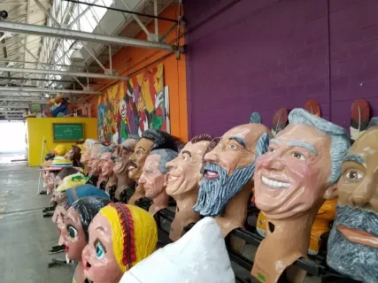 Large colorful puppet heads lined up on shelves in a vibrant warehouse.