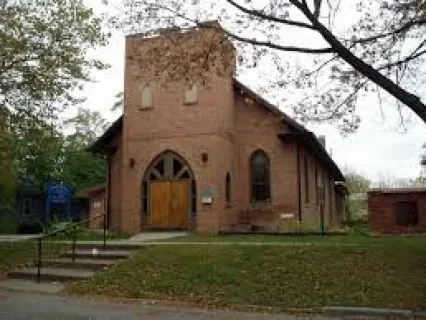 Historic brick church with arched wooden doors, surrounded by trees.