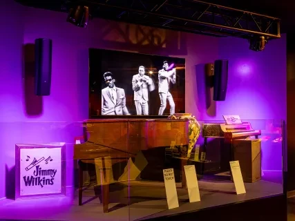 Stage with purple lighting, vintage piano, and a screen showing black and white performers.