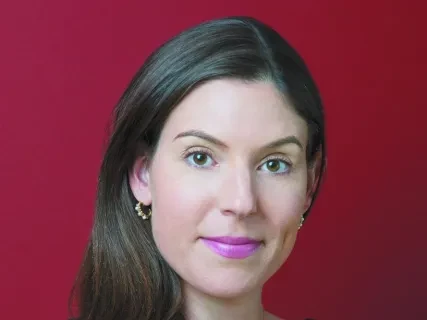 Woman with long brown hair, wearing a black top, against a red background.