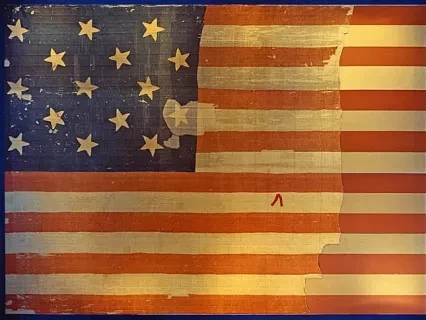 Faded American flag with 15 stars and stripes, showing signs of wear and age.