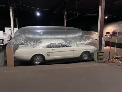 Vintage white car stored in a transparent bubble cover inside a dimly lit warehouse.