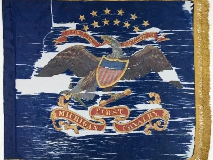Historic blue cavalry flag with an eagle and shield, surrounded by stars, and text "First Michigan Cavalry" on banners.