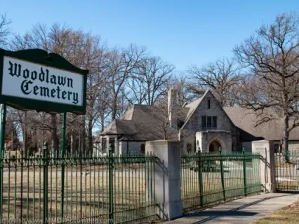 Woodlawn Cemetery entrance with a historic stone building and leafless trees on a clear day.