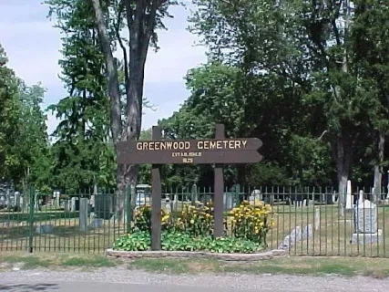 Entrance sign for Greenwood Cemetery, surrounded by yellow flowers and trees.