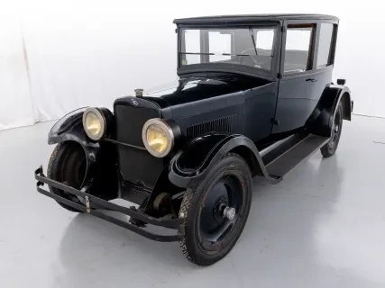 Dark vintage car with round headlights in a white studio setting.