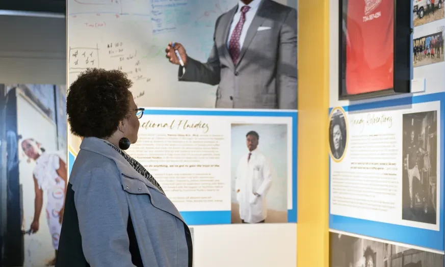 Woman observing a museum exhibit with portraits and informational panels.