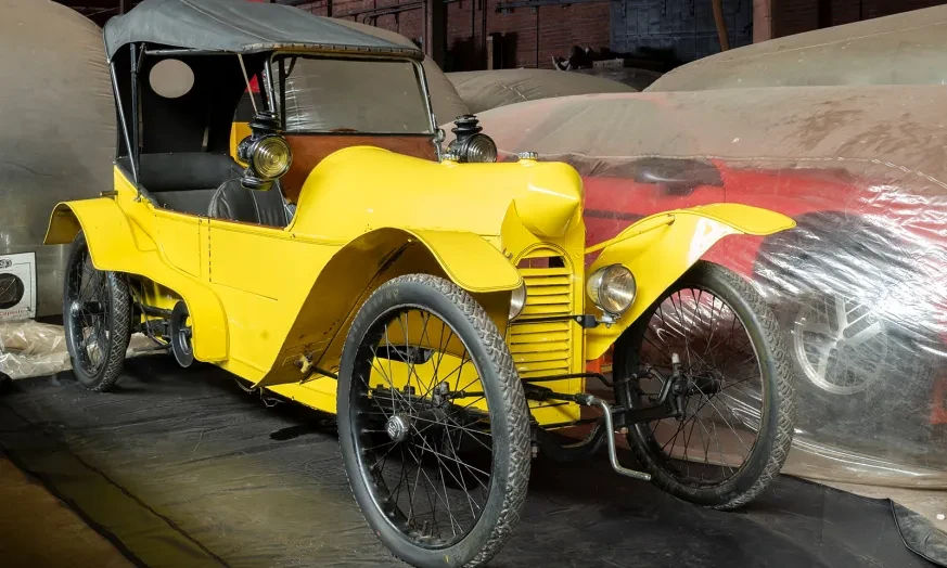 Yellow vintage car with three wheels in a dimly lit garage.