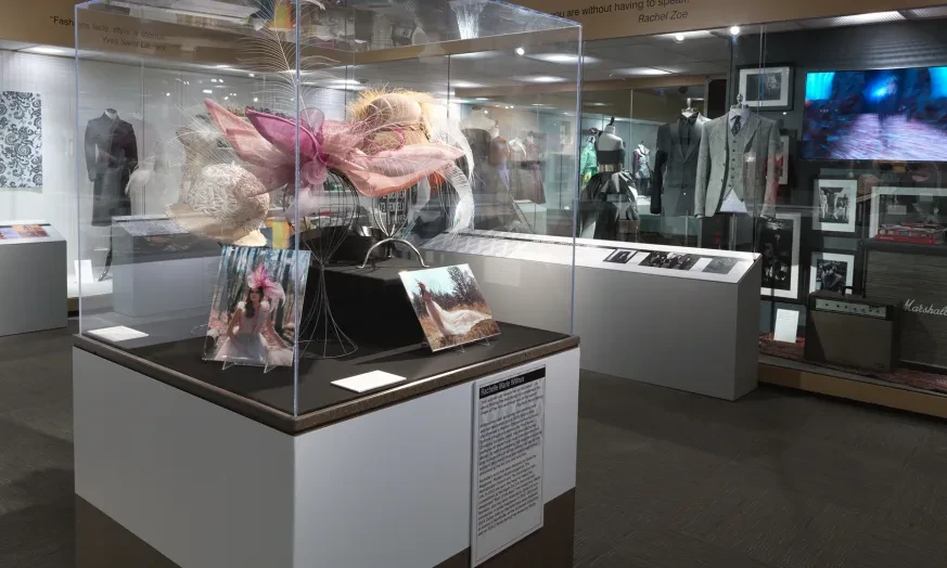 Museum exhibit with colorful sculpture in glass case, surrounded by photographs and displays on modern clothing.