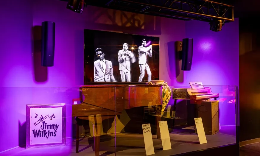 Stage with purple lighting, vintage piano, and a screen showing black and white performers.
