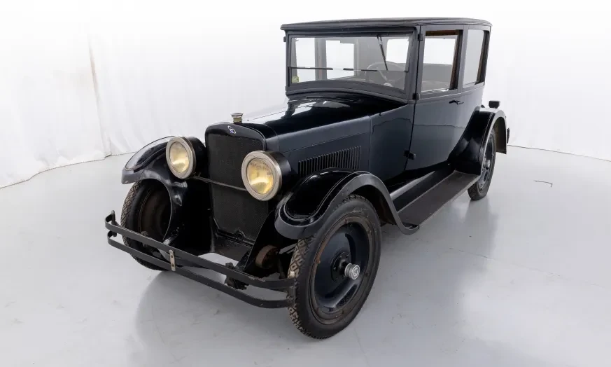 Dark vintage car with round headlights in a white studio setting.