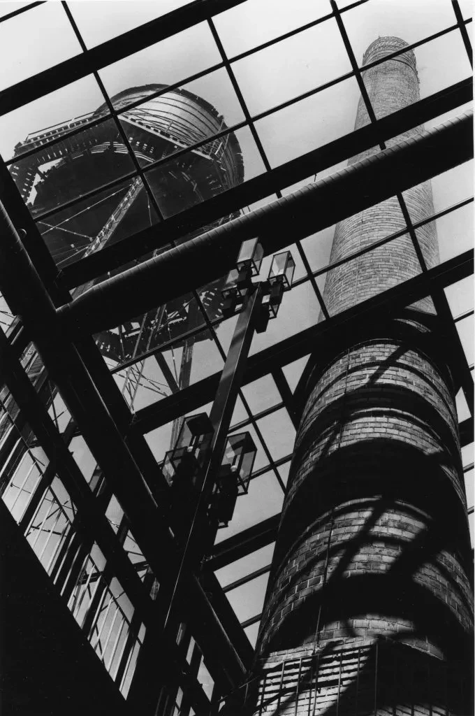 View of industrial towers through a glass roof with geometric patterns, in black and white.