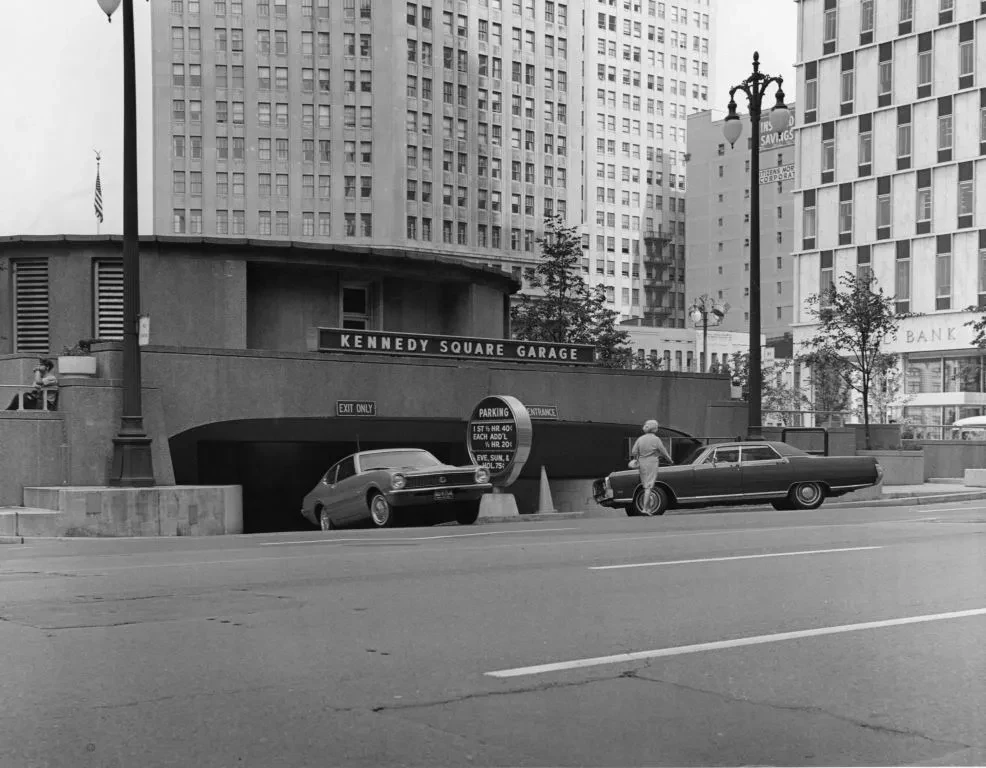 Downtown street scene with cars exiting a tunnel, surrounded by tall buildings. Black and white photograph.