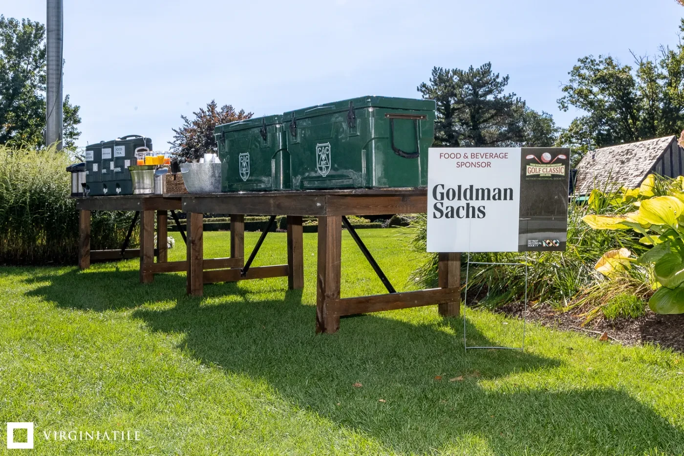 Large green storage boxes on a wooden table outdoors, next to a Goldman Sachs sign.