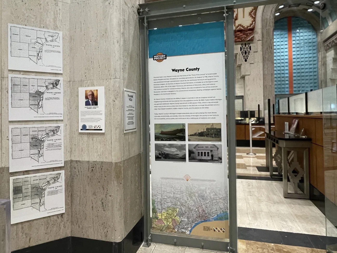 Display panel in a hallway with maps and text about Wayne County. Contains historical photos and maps on the left wall.
