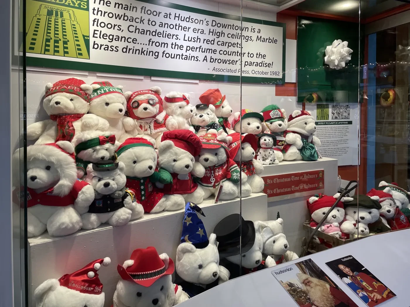 Teddy bears in festive hats and scarves displayed in a glass case.