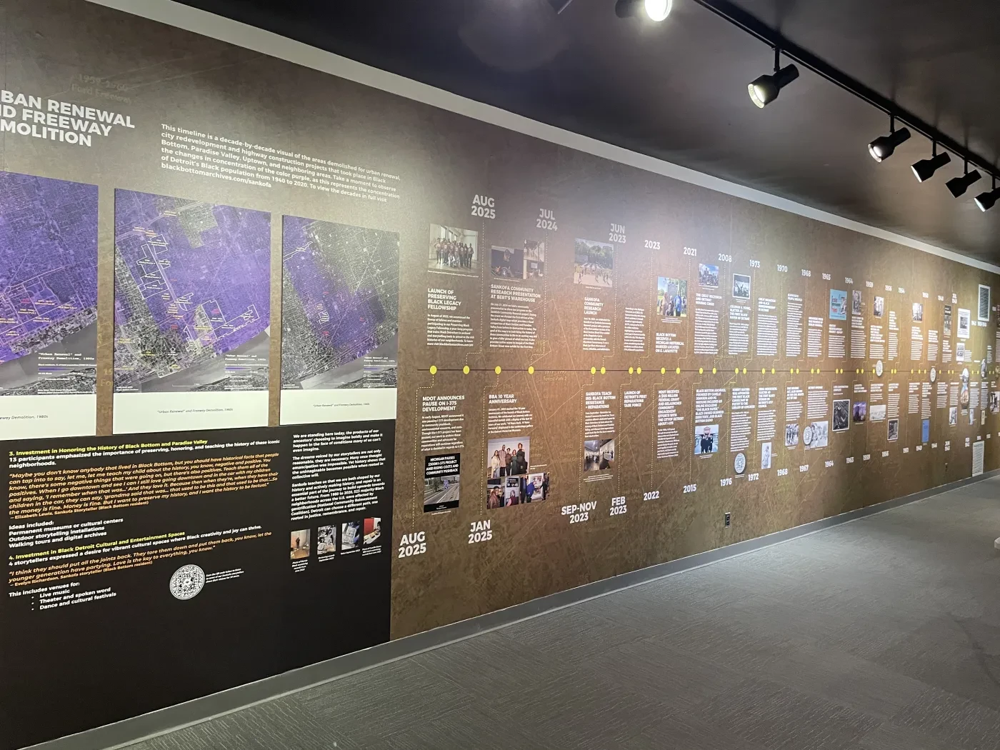 Exhibit wall with timeline, photographs, and text under spotlights in a museum setting.
