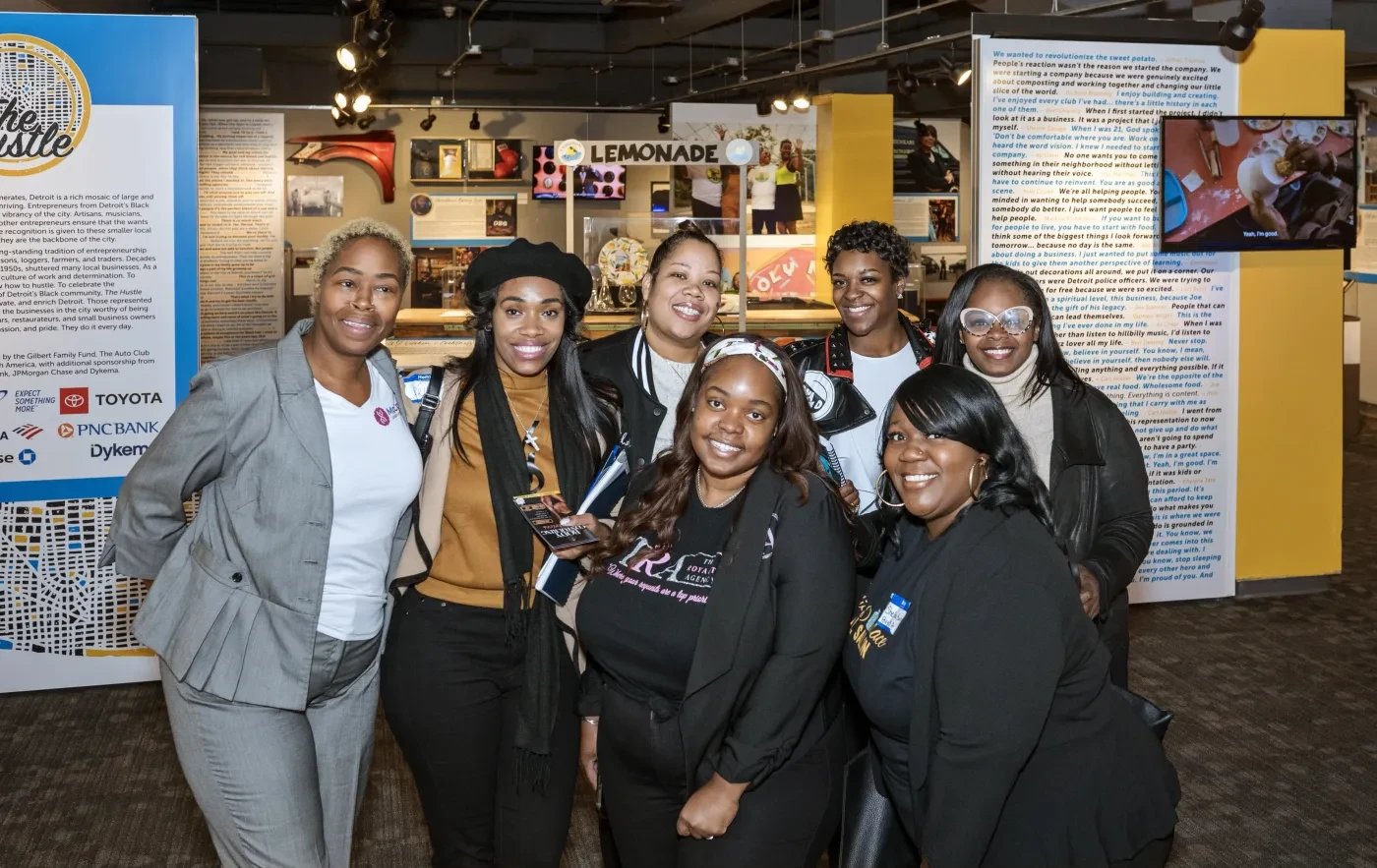 Group of eight smiling people in a brightly lit room with informational displays in the background.