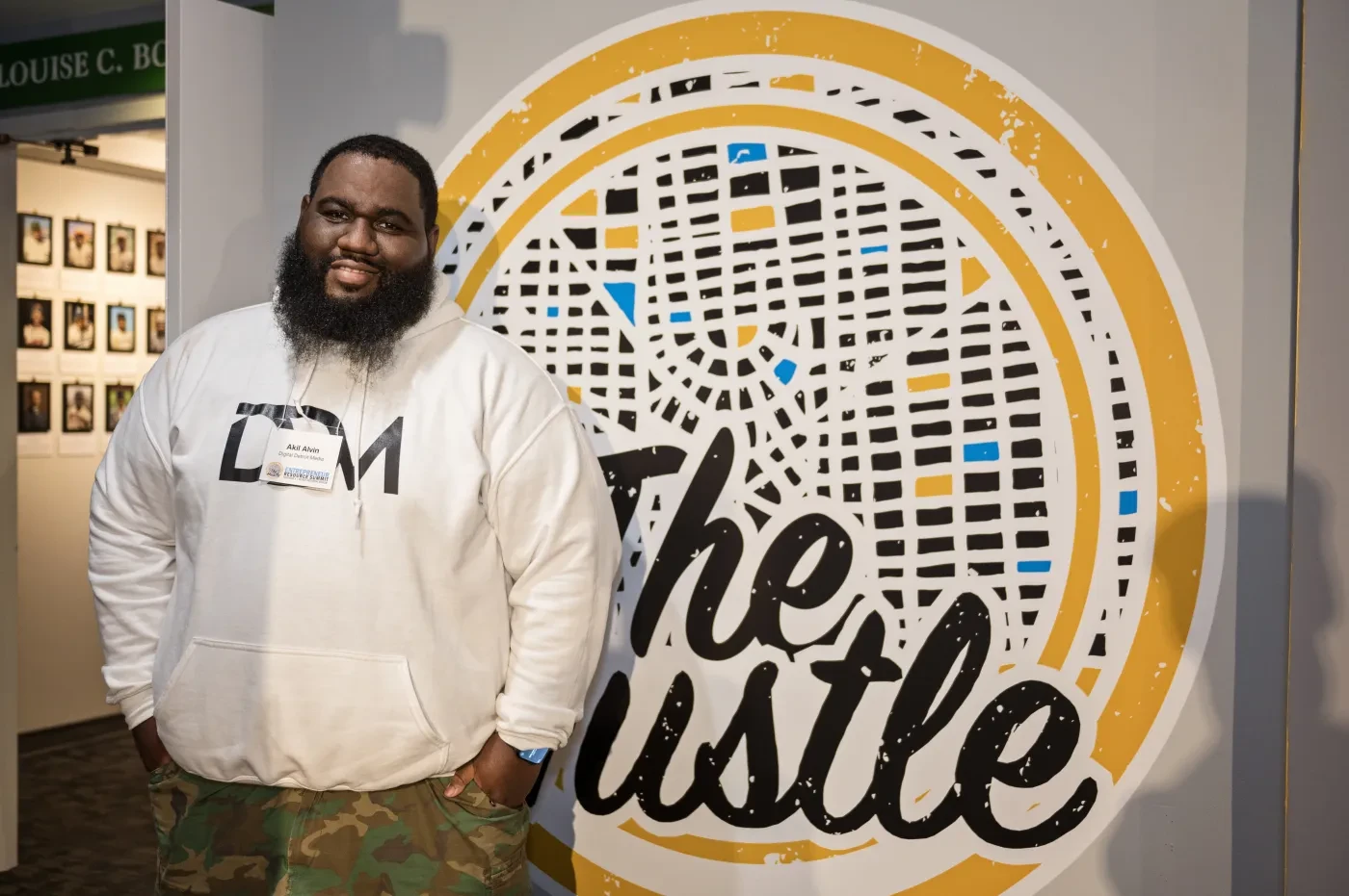 Man smiling in front of a colorful mural with the text "The Hustle."