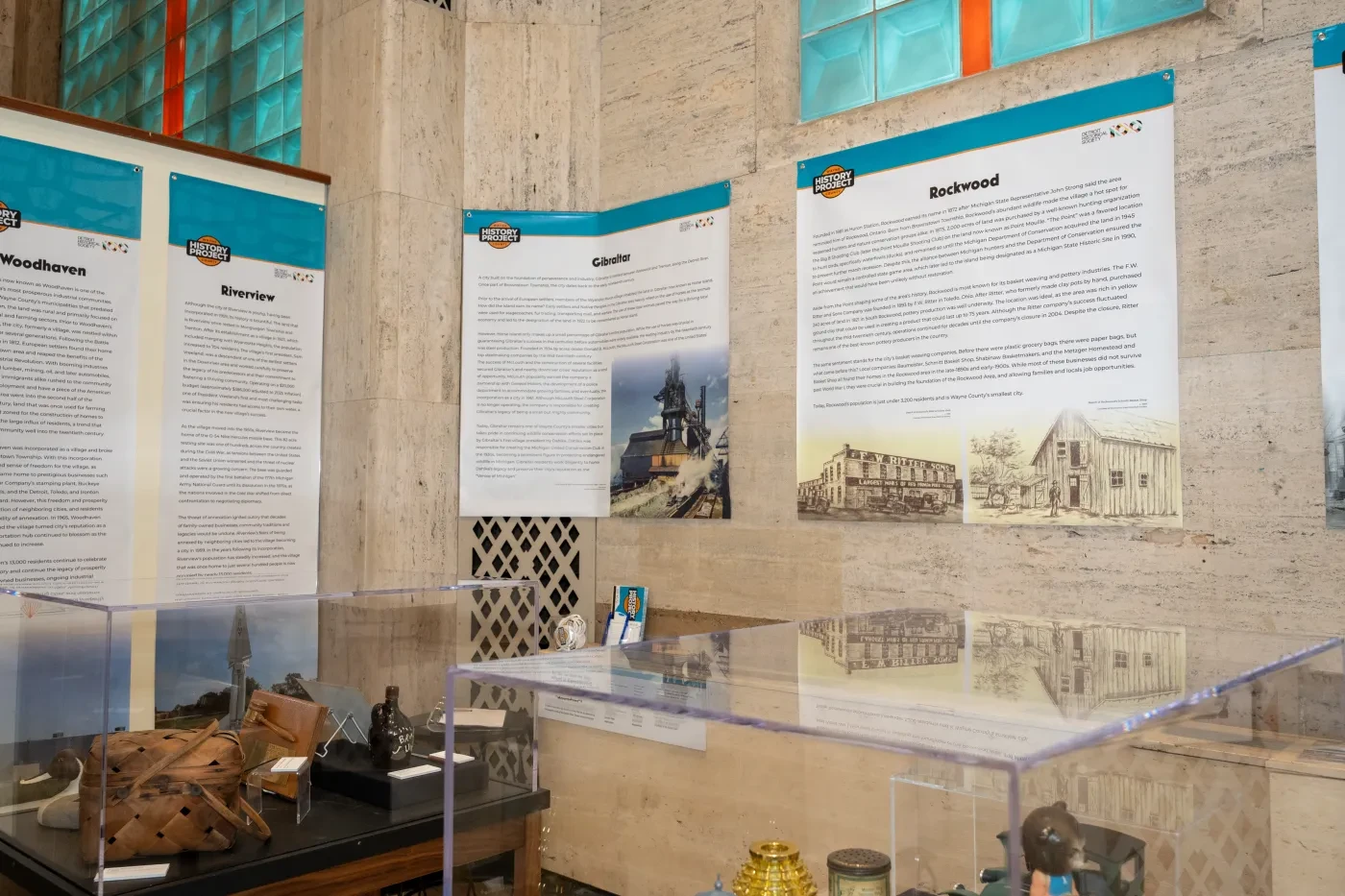 Museum exhibit with informational panels and artifacts in glass cases, set against a stone wall.