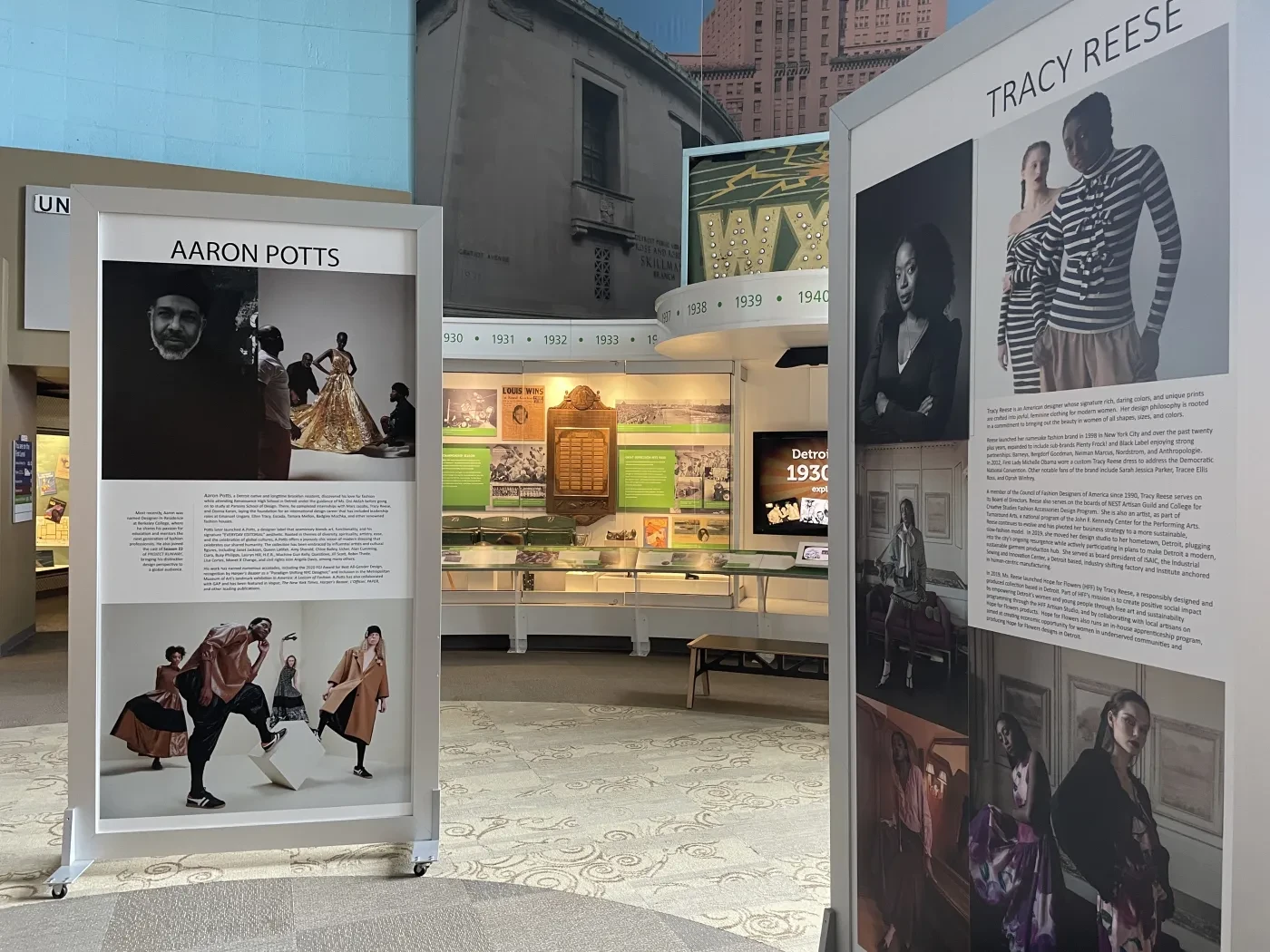 Museum exhibit with curated fashion displays, featuring mannequins and photographs, under soft lighting in a spacious interior.