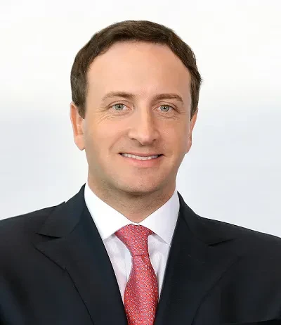 Smiling man in a suit with a red tie, set against a plain background.